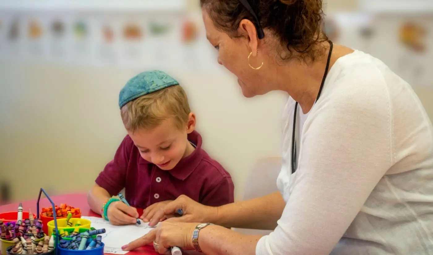 Teacher at eye level with a child, noticing and celebrating effort.