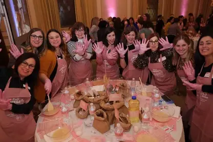 Smiling women in pink aprons and gloves with hands raised