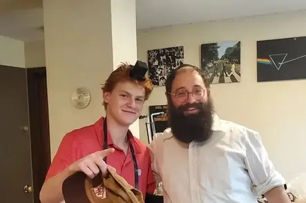 Two men, one younger, one older with a beard and cane, both wearing skullcaps.