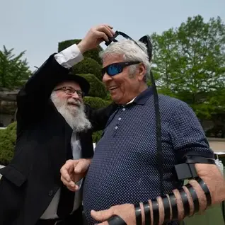 Rabbi helps smiling man put on tefillin