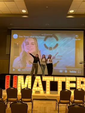 Three young women on stage in front of a screen and 'I MATTER' sign.