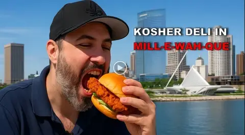 Man eating a kosher deli sandwhich in front of the Milwaukee skyline