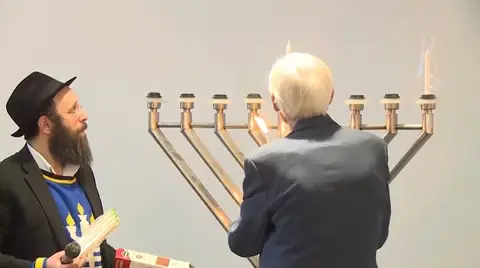 Man lighting the Menorah with a Rabbi overseeing.