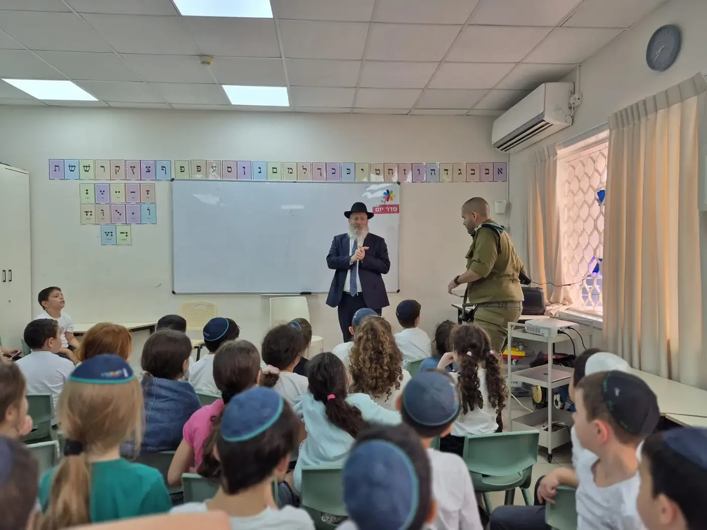 תלמידים יושבים בכיתה ומקשיבים למפגש, על הקיר אותיות האלף־בית