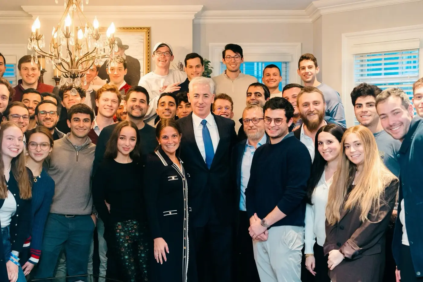 Group of people gathered for a photo indoors, with a chandelier and framed picture hanging on the wall behind them.