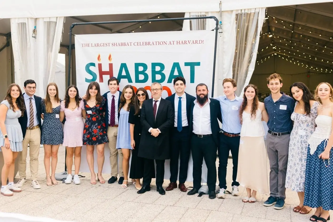 Group of people standing in front of a sign that reads 'The Largest Shabbat Celebration at Harvard! Shabbat.'