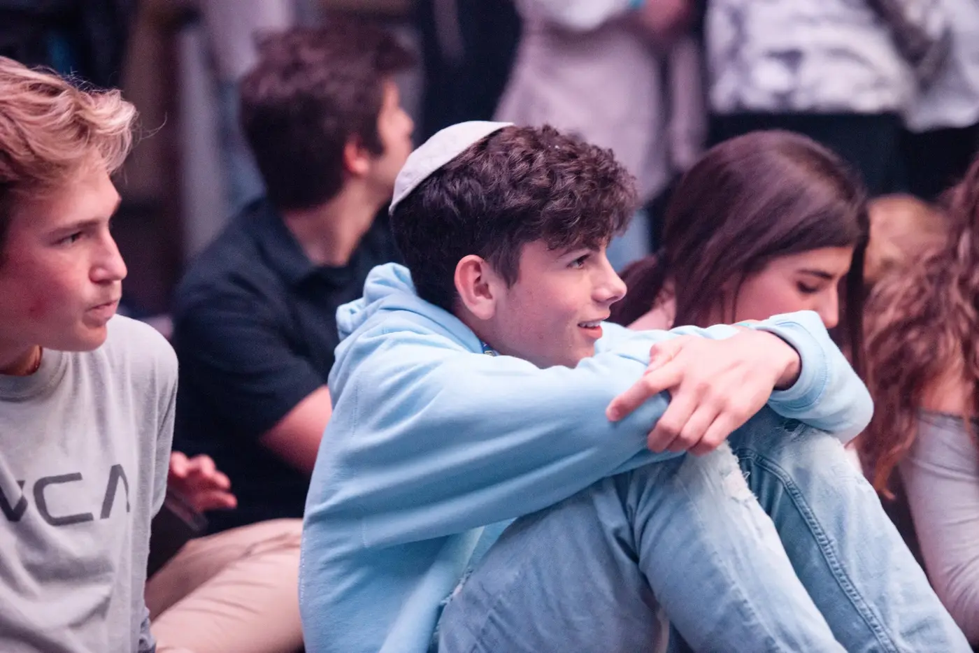 Young people sitting on the floor, listening attentively at an indoor event.