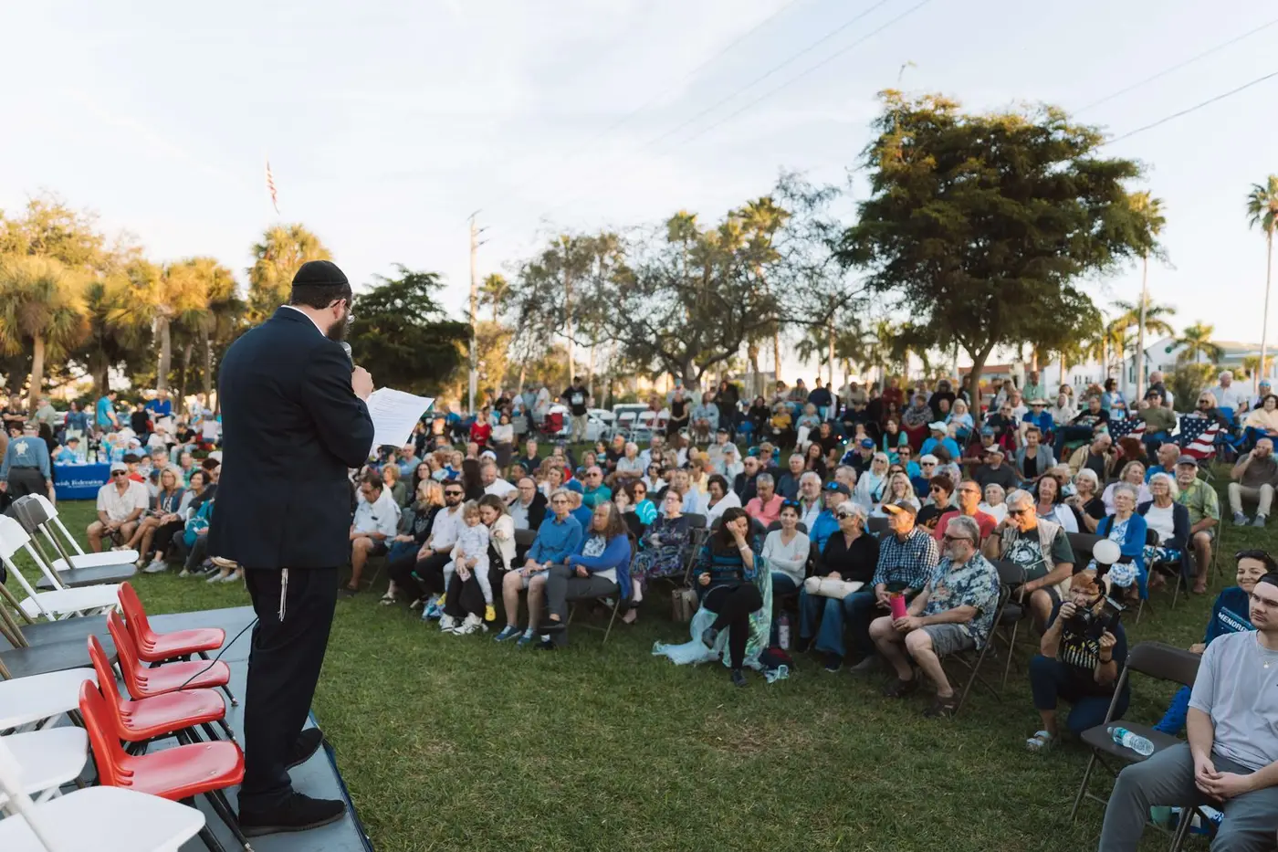 Rabbi Sholom Schmerling addressing a large community crowd at an outdoor gathering