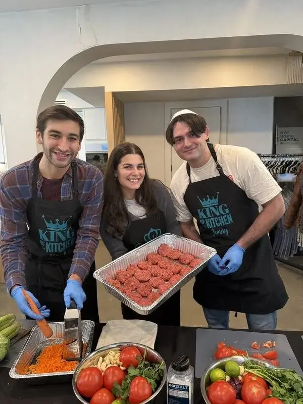 Three volunteers in King of the Kitchen aprons holding up a tray of hand-rolled meatballs