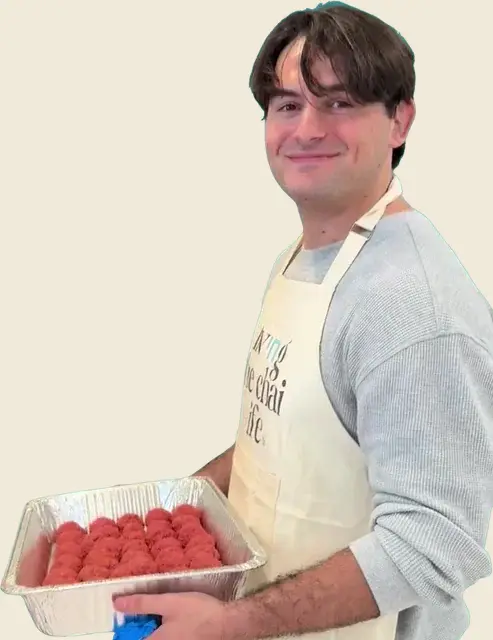 Johnny Ellis, smiling in an apron while holding a tray of meatballs he rolled by hand