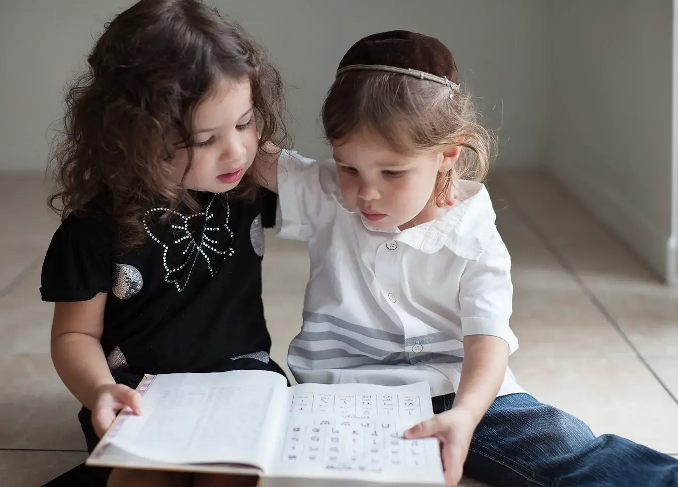 Two young Jewish children reading a Hebrew book together