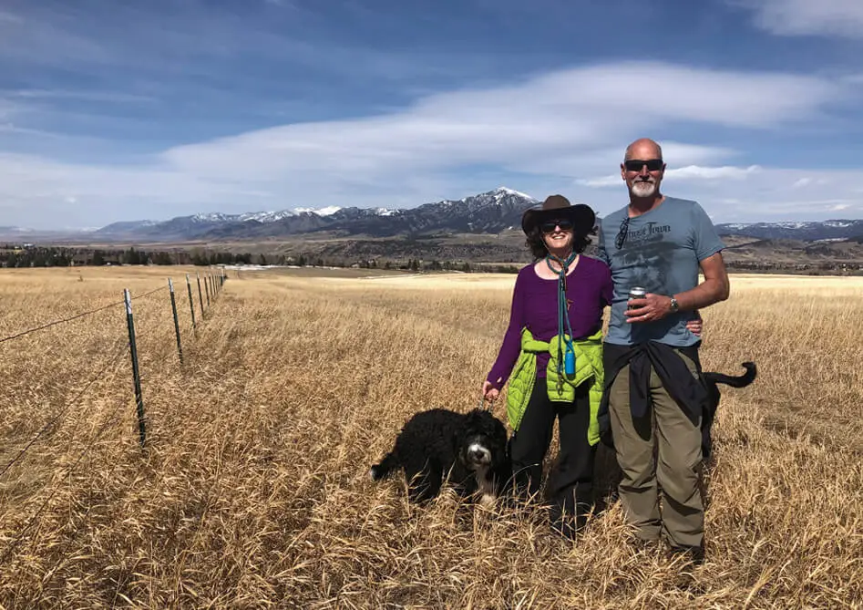 Sarah, Rob, and their dog Nola in a field behind their home with the Bridger Mountains in the background.