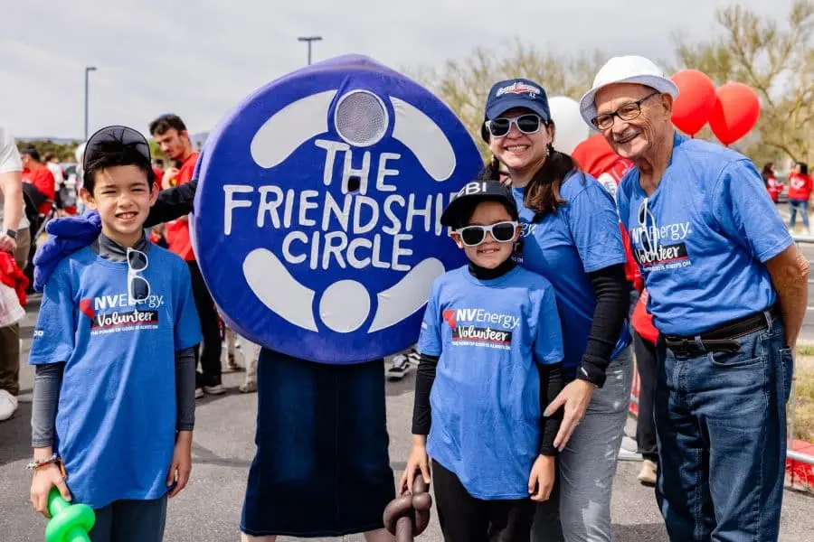 Four people in blue "NVEnergy Volunteer" shirts stand next to a large blue sign that says "THE FRIENDSHIP CIRCLE."