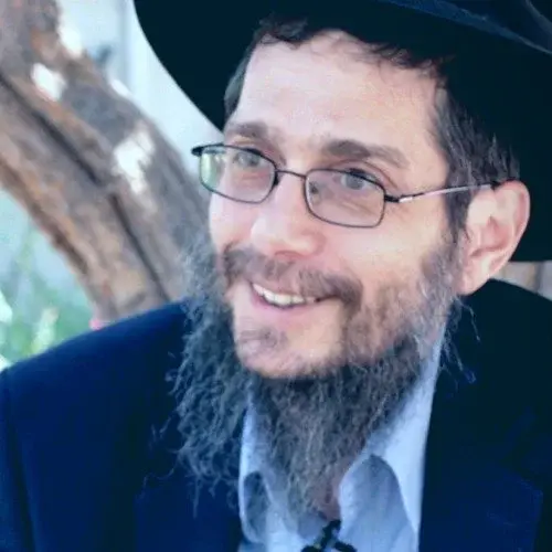 A man with glasses, a beard, and a mustache wearing a black hat and a dark jacket, smiling outdoors near a tree.