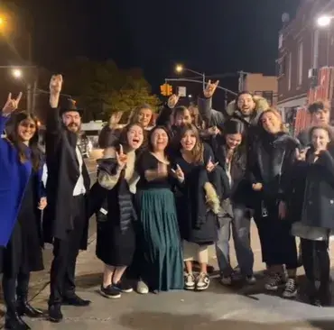 Group of people posing joyfully on a city street at night.