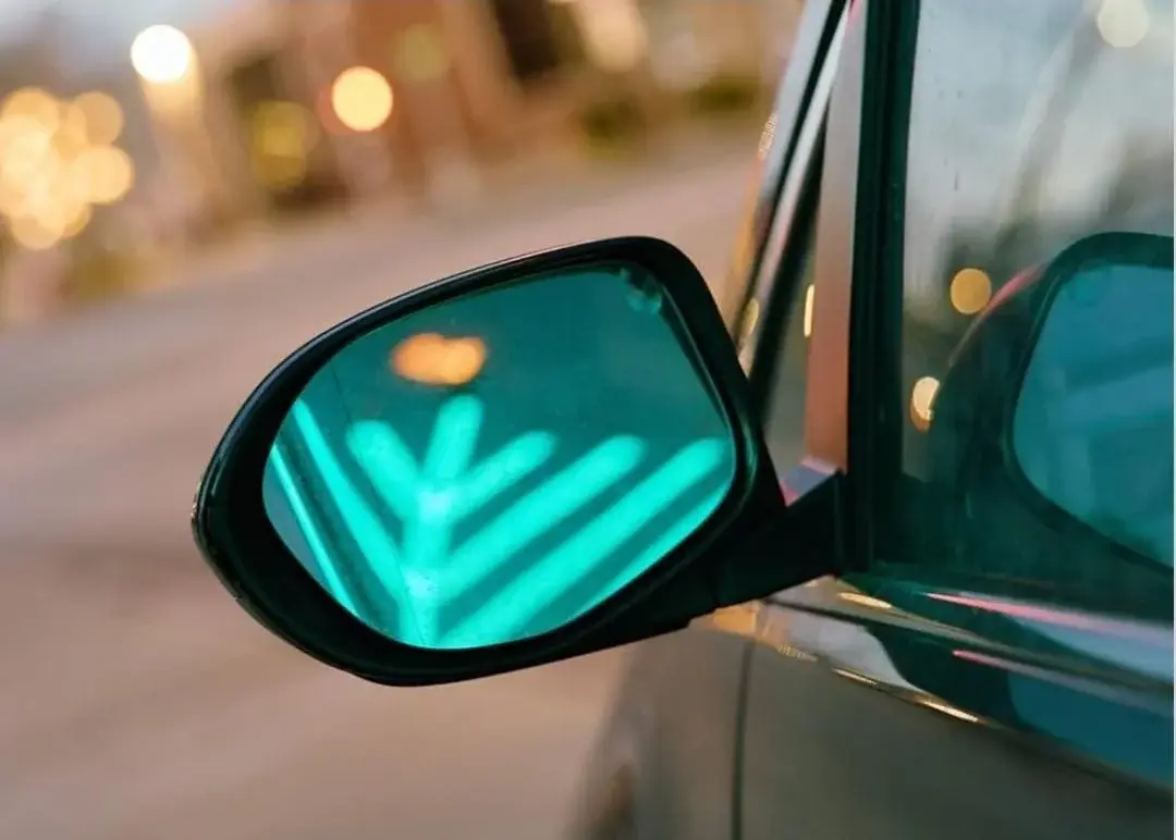 Car side mirror reflecting a green arrow turn signal
