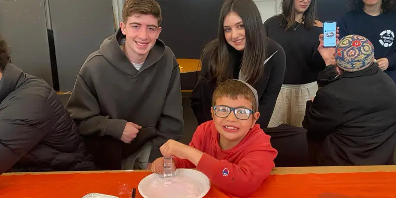 Group of three individuals participating in a hands-on activity, focusing on a young boy in a red shirt.