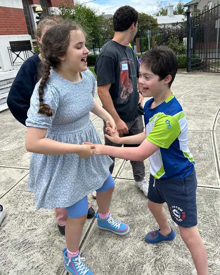 Two children smiling while holding hands and dancing outdoors.
