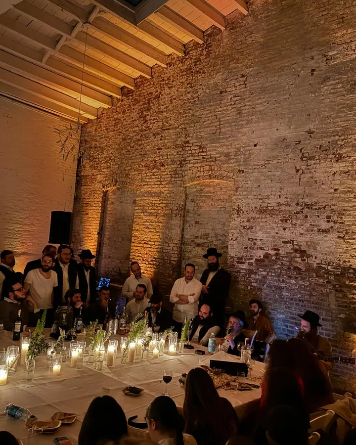 People gathered around a long table with lit candles and decorations, in a rustic brick-walled venue during a social event or dinner.