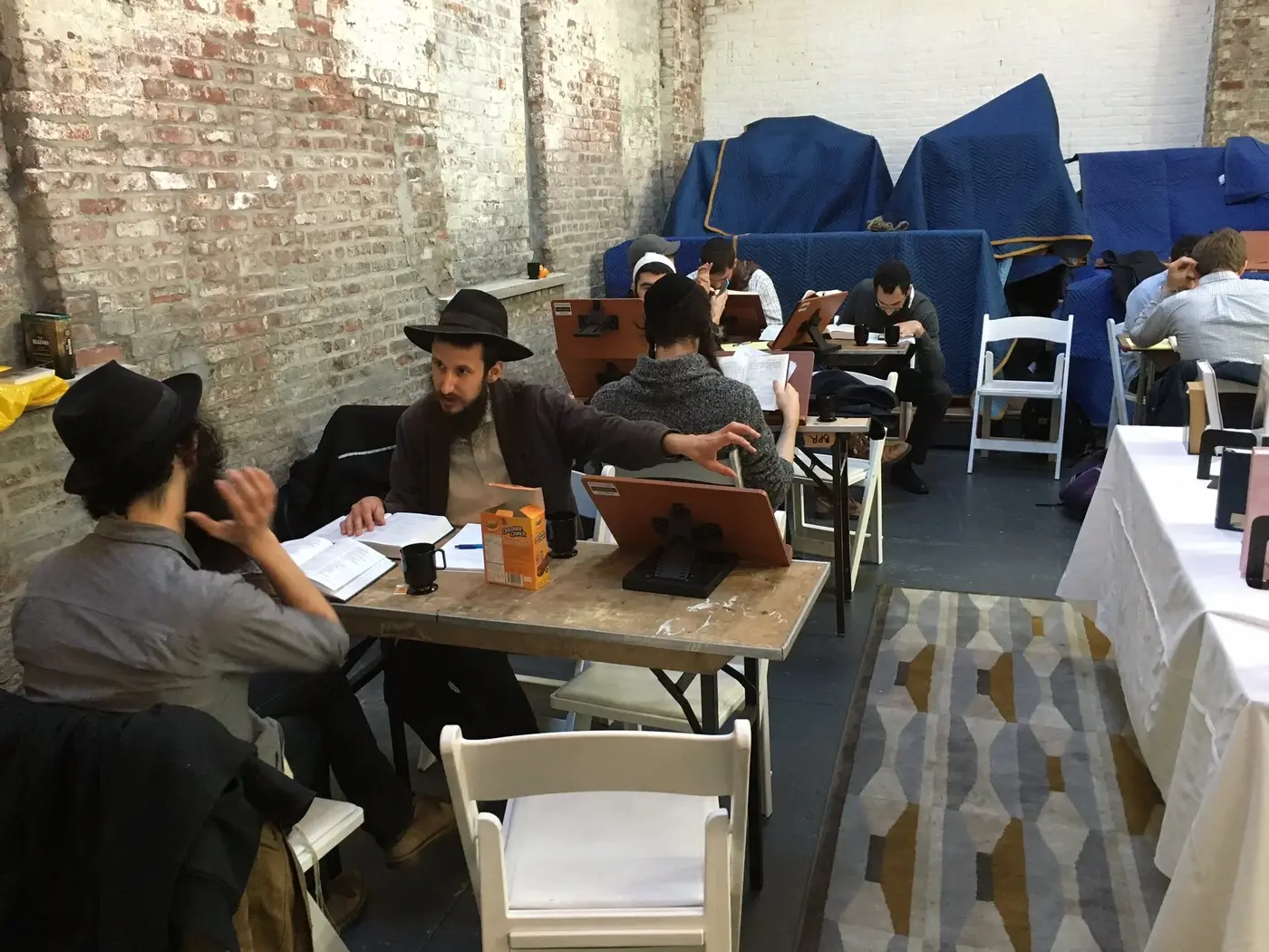 People studying and reading at a cafe or workspace with exposed brick walls and covered furniture in the background.